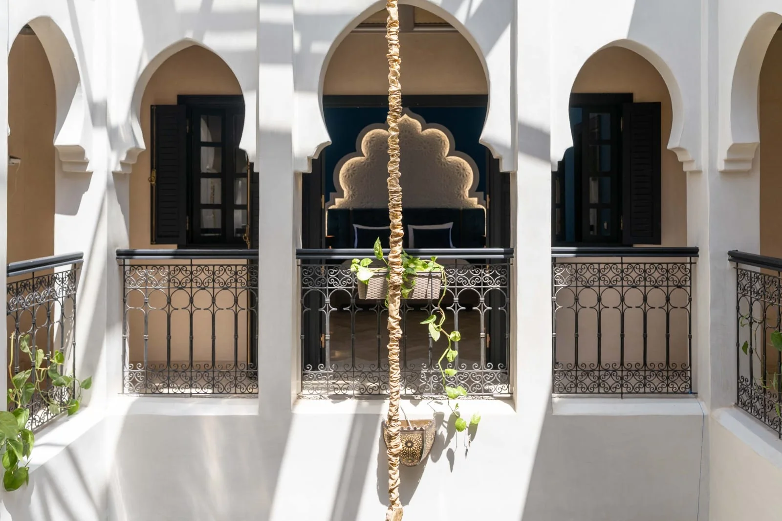 White upstairs arches framing the blue bedroom, with plants and wrought-iron patio railings